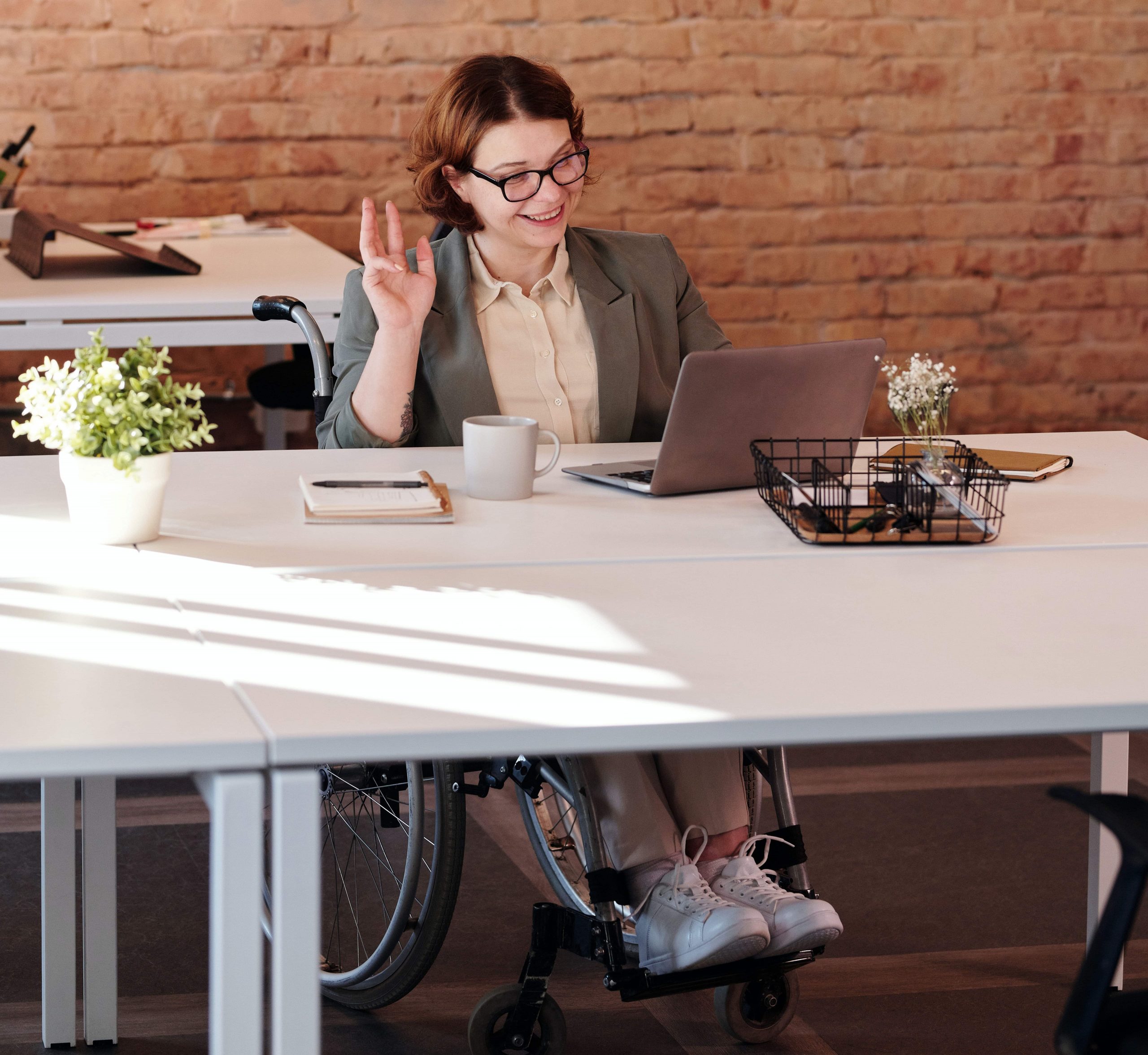 Woman in wheelchair sitting at desk and waving at laptop