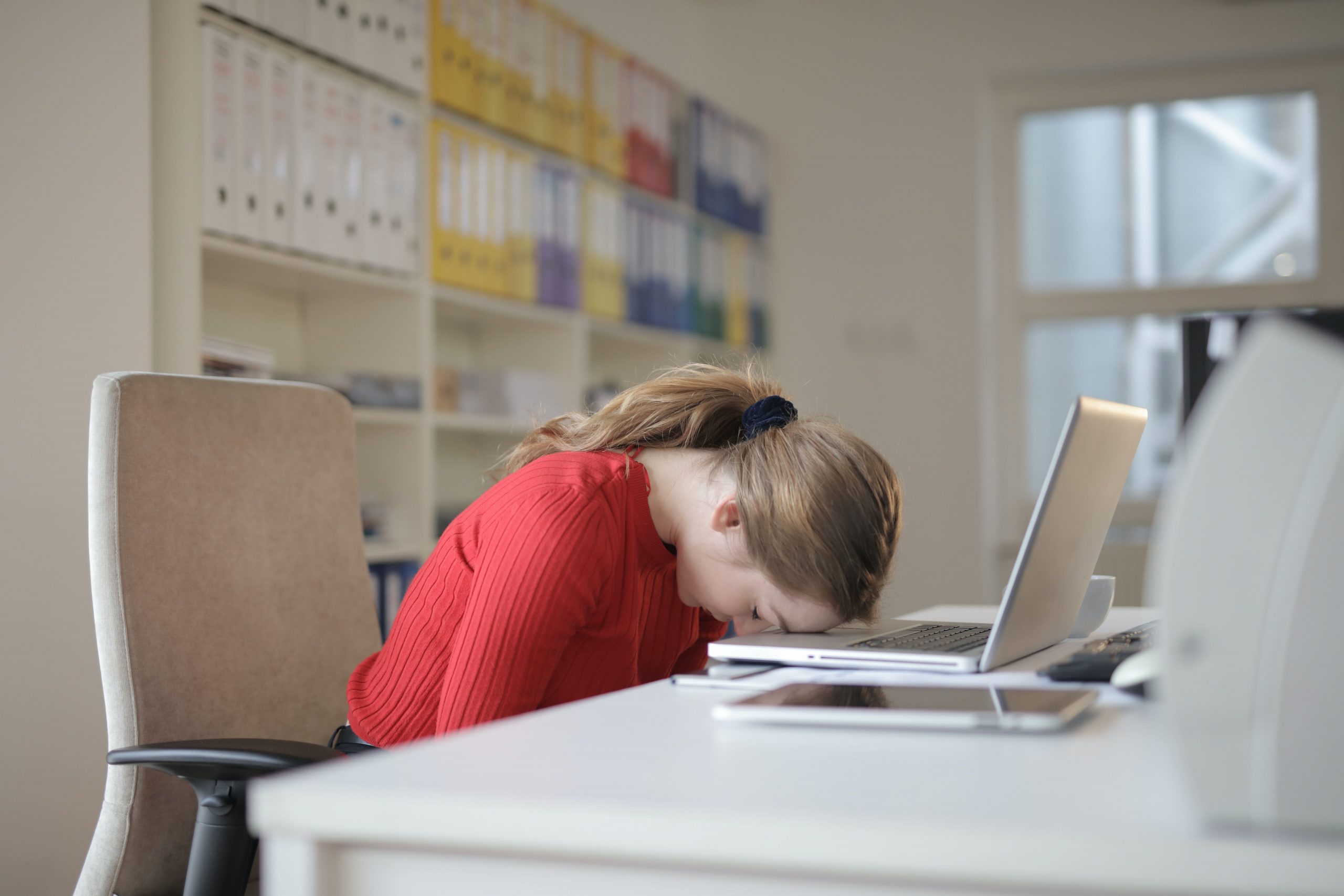 Insurance agent resting head on desk with laptop due to problems in the workplace